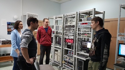  W laboratorium czasu, gdzie widocznych jest wiele serwerów oraz komputerów mężczyzna opowiada coś kobiecie i mężczyźnie. Obok stoi drugi mężczyzna.