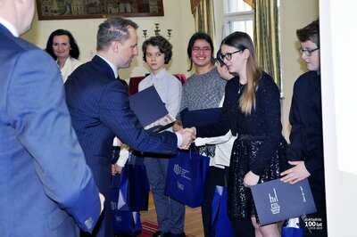  Mężczyzna (Prezes Maciej Dobieszewski) wręcza młodym ludziom (nastolatkom) torby firmowe Głównego Urzędu Miar.