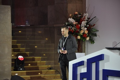 dr hab. Andrzej Dragan Mężczyzna w szarej marynarce stoi przy mównicy. Za nim w wielkim wazonie kwiaty.