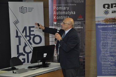Dr Władysław Kozłowski z Laboratorium Chemii GUM dr Władysław Kozłowski z Laboratorium Chemii GUM wskazuje wskaźnikiem istotny fragment w swojej prezentacji - starszy mężczyzna z mikrofonem w drugiej ręce. Za nim widać stojące roll-upy, które informują o wydarzeniu.
