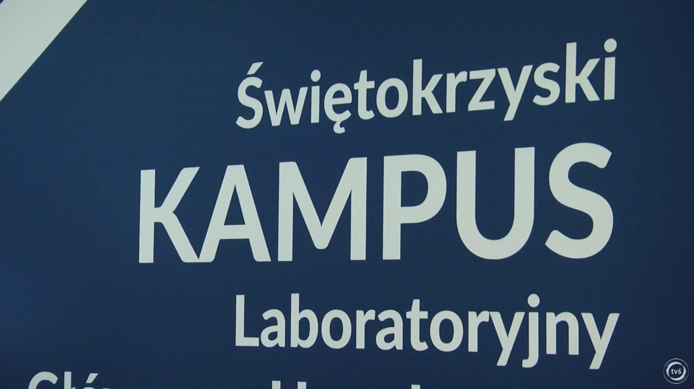 Kadr z relacji filmowej: zbliżenie na duży roll-up lub plakat z napisem Świętokrzyski Kampus Laboratoryjny na granatowym tle. 